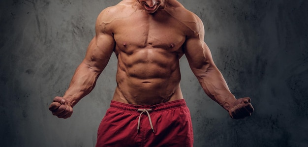 Muscular man with nice muscules is posing for photographer at dark photo studio.