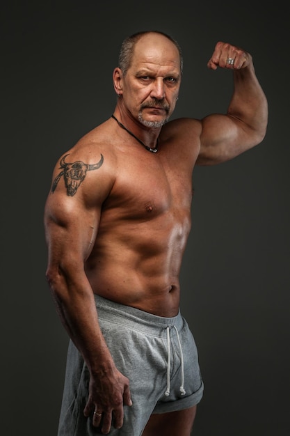 Muscular middle age man posing in studio. Isolated on grey