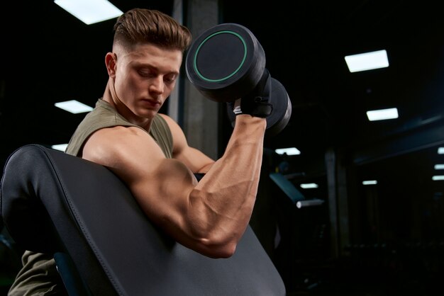 Muscular sportsman building biceps with dumbbell.