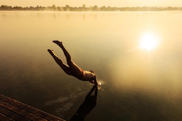Muscular sportsman plunging into lake from wooden pier