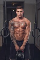 Muscular tattooed man holds lifting weight.