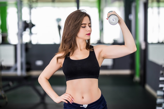 Muscular woman working out in fitness centre with two dumbbells