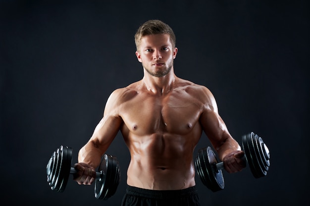 Muscular young man lifting weights on black background