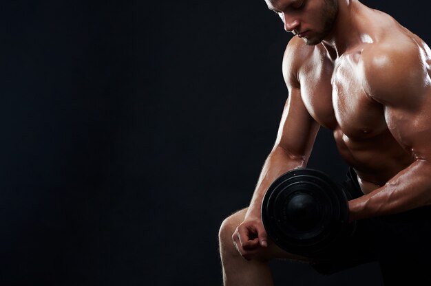 Muscular young man lifting weights on black background