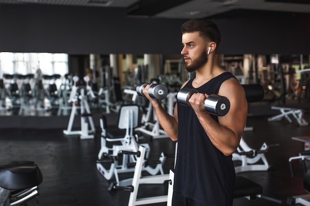 Giovane muscolare che si allena in palestra facendo esercizi con manubri al bicipite