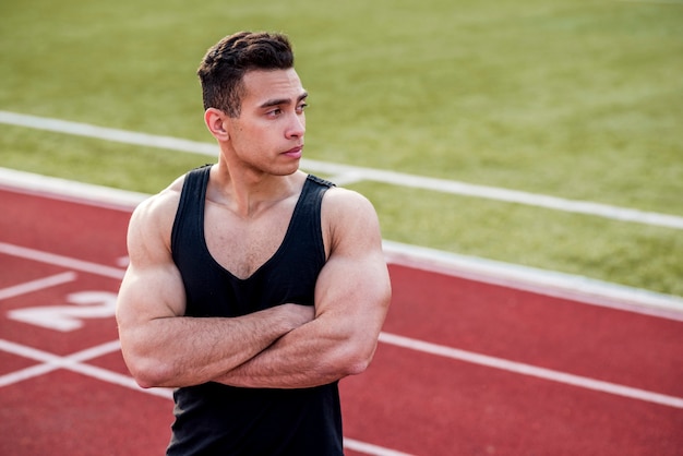 Il giovane sportivo muscolare con il suo braccio ha attraversato la condizione sulla pista di corsa