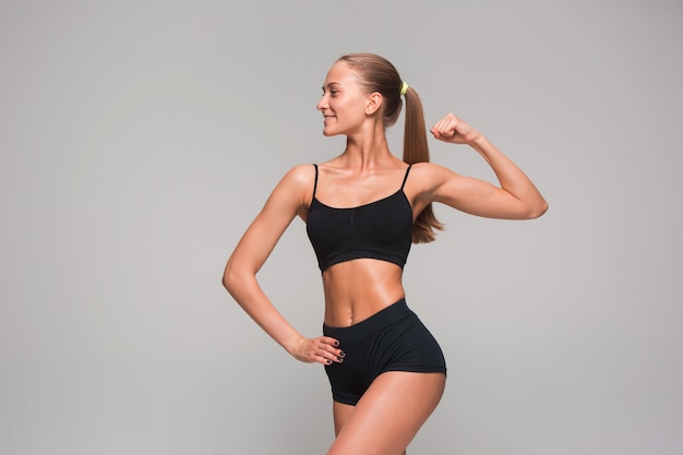 Muscular young woman athlete on gray