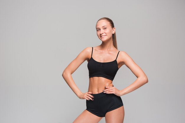 Muscular young woman athlete posing on gray