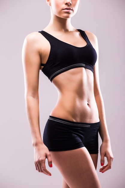 Free photo muscular young woman athlete standing looking down with her hands on hips on grey wall