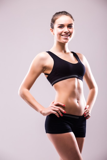 Muscular young woman athlete standing looking down with her hands on hips on grey wall