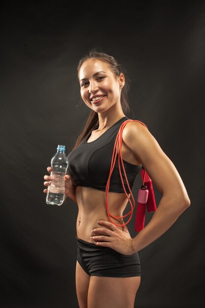 Muscular young woman athlete with a skipping rope on black