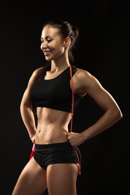 Muscular young woman athlete with a skipping rope on black