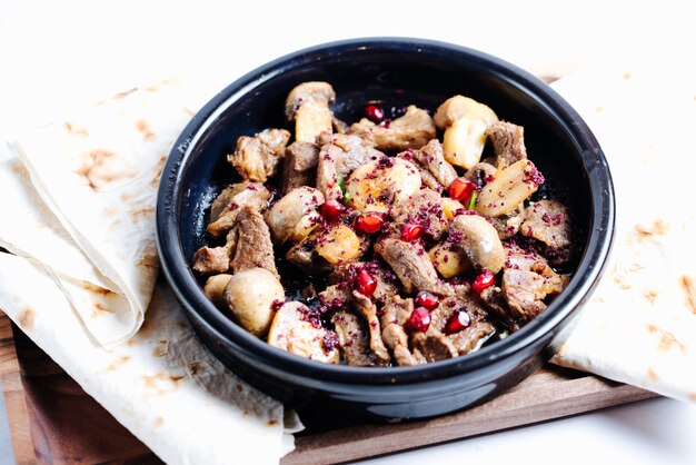 mushroom and meat slices in pot topped with pomegranate