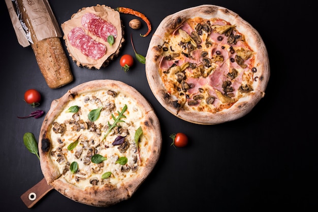 Foto gratuita pizza di funghi e salumi con ingredienti disposti su una superficie nera