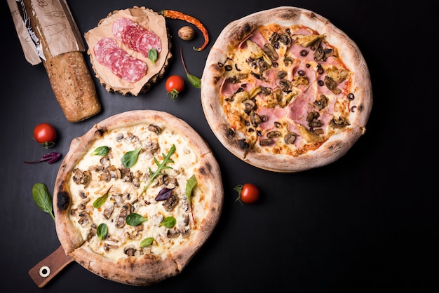 Mushroom and salami pizza with ingredients arranged over black surface