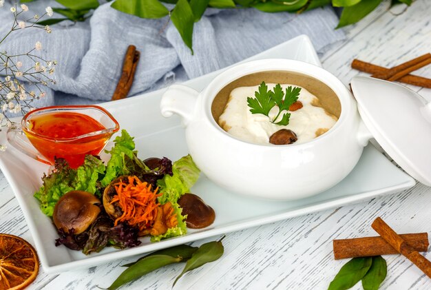 Mushroom soup in ceramic serving ware served with salad and sauce