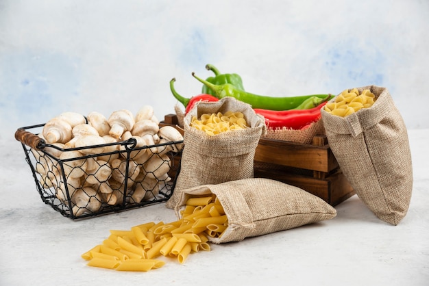 Mushrooms, chili peppers and pastas in rustic basket on white table.