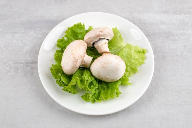 Mushrooms on a lettuce leaf on a plate, on the marble table. 