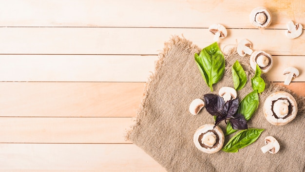 Mushrooms with leafy vegetable on jute sack over the wooden plank