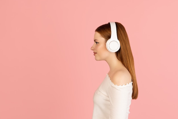 Music. Caucasian woman's portrait isolated on pink  wall with copyspace for ad. Beautiful woman with headphones. Concept of human emotions, facial expression, youth culture.