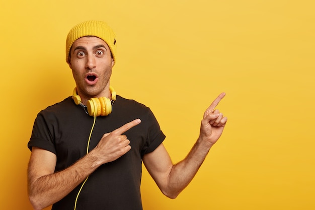 音楽はテクノロジーの一部です。驚いた白人男性は、ヘッドフォン、黄色のヘッドギア、黒のTシャツを着ています