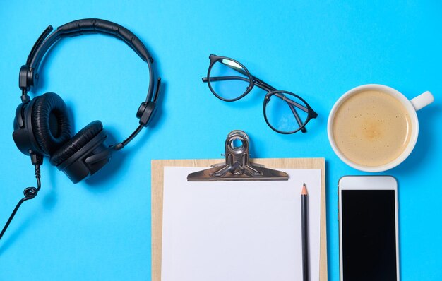 Music or podcast background with headphones microphone coffee and blank on blue table flat lay Top view flat lay