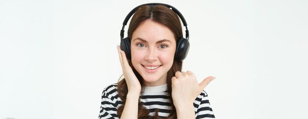 Music store concept smiling young woman listening song in headphones pointing left at copy space