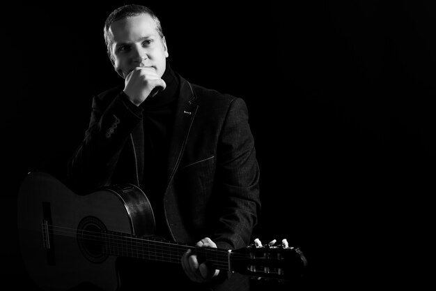 Music. Young musician in black suit holding a guitar