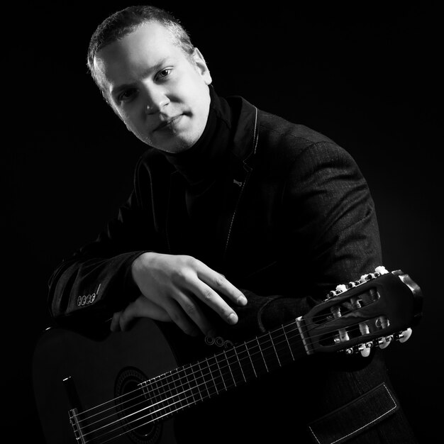 Music. Young musician in black suit holding a guitar