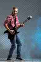 Free photo music. young musician with a guitar on fence wall