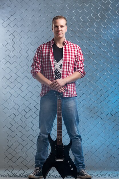 Music. Young musician with a guitar on fence wall