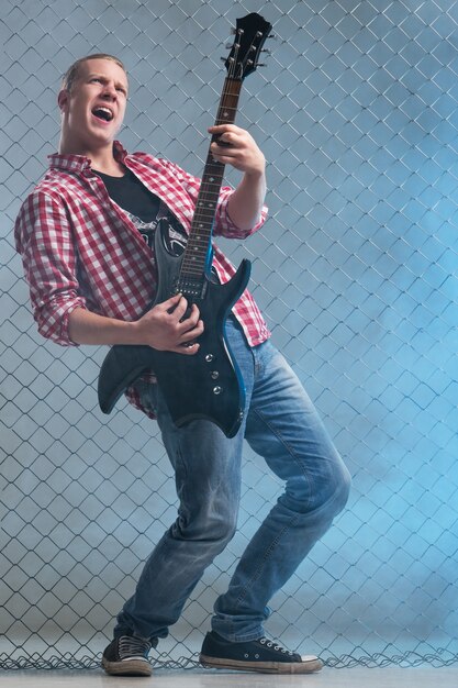 Music. Young musician with a guitar on fence wall