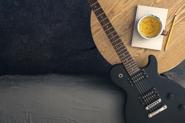 Free photo musical background with electric guitar notepad and cup of tea on the table