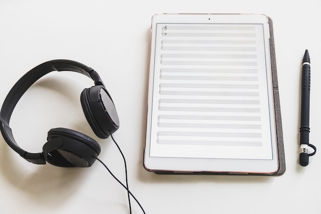 Musical note on digital graphic tablet; stylus pen and headphone on white background