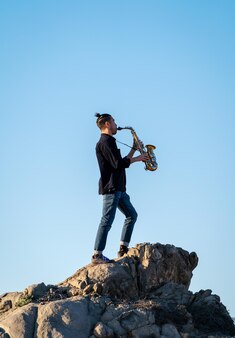 ミュージシャンは岩の上に立って、砂漠の日没時にサックスを演奏しています