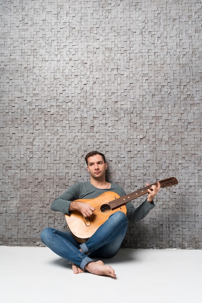 Бесплатное фото Музыкант опирается на стену и играет на гитаре