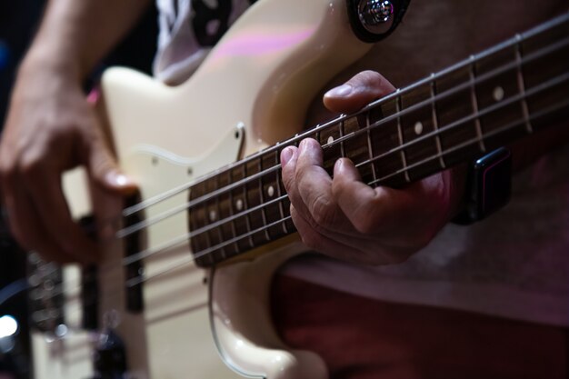 Musician playing white bass guitar close up.