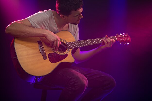 ミュージシャンはアコースティックギターを弾きます。美しい色の光線。