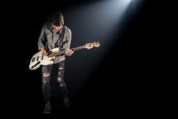 the musician plays bass guitar, on a black background with a beam of light, emotional play, music concept