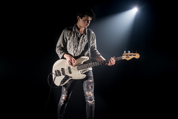 the musician plays bass guitar, on a black background with a beam of light, emotional play, music concept