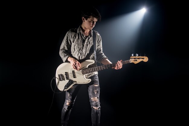 the musician plays bass guitar, on a black background with a beam of light, emotional play, music concept