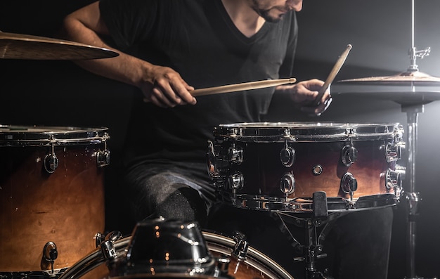 A musician plays drums with sticks on stage with stage lighting.