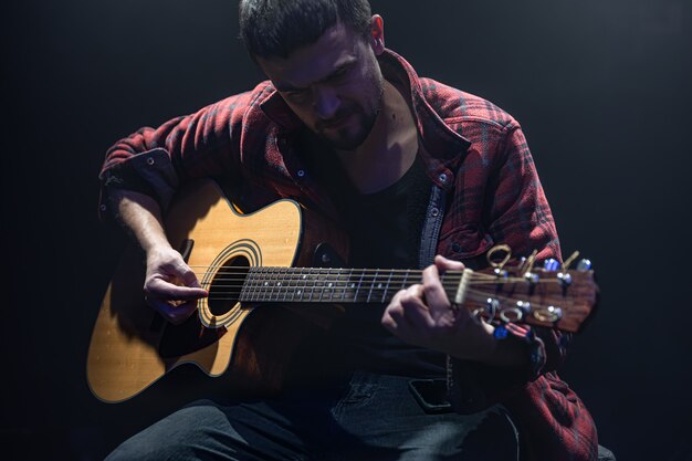 음악가는 어두운 방에 앉아 기타를 연주합니다.