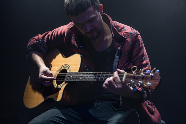 음악가는 어두운 방에 앉아 기타를 연주합니다.