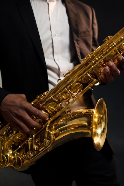 Музыкант в костюме держит саксофон крупным планом