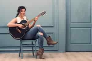 Free photo musician with guitar sitting on chair