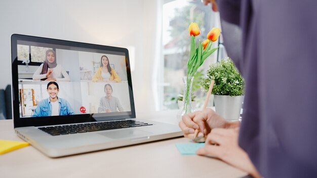 muslim businesswoman using laptop talk to colleague about plan by video call brainstorm online meeting while remotely work from home at living room.