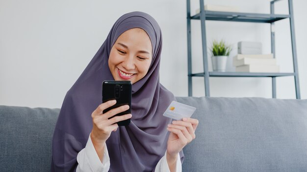 мусульманская женщина пользуется смартфоном, покупает кредитную карту и покупает интернет-магазин в гостиной дома.