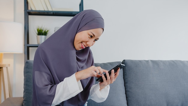 이슬람 여성은 스마트 폰을 사용하고 집 거실 소파에서 전자 상거래 인터넷을 구입합니다.