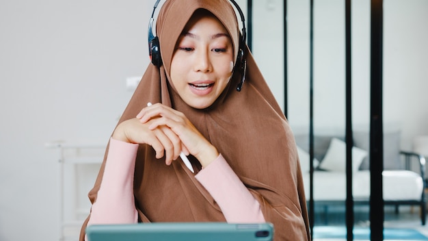 Free photo muslim lady wear headphone using digital tablet talk to colleagues about sale report in conference video call while working from home at kitchen.